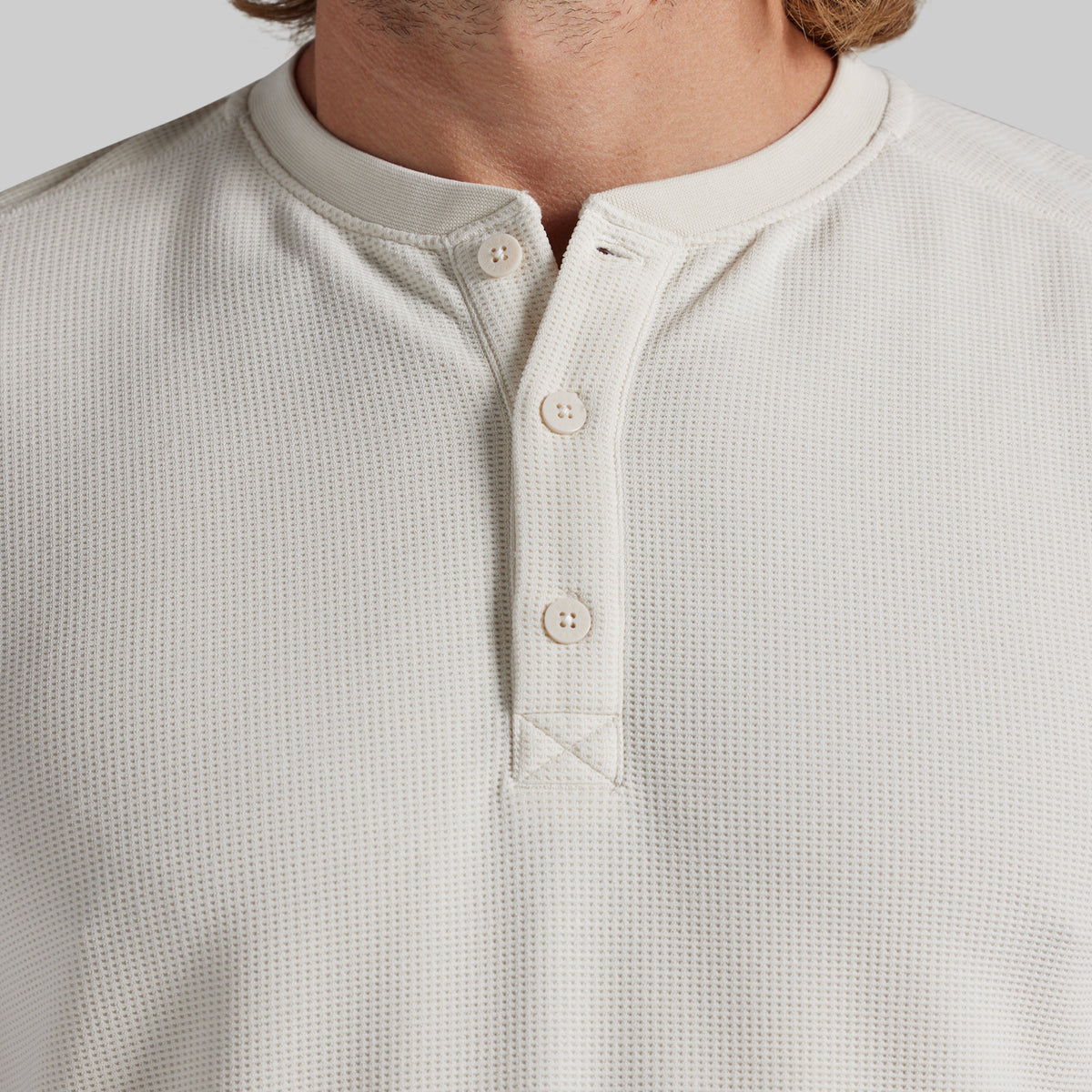 Close-up of a man wearing a textured waffle-knit henley shirt in off-white/cream with a three-button placket.