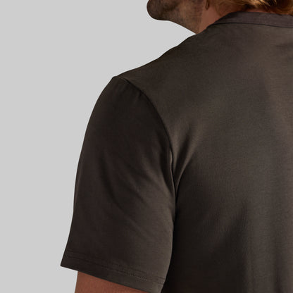 Close-up of a person wearing a dark brown short-sleeve crewneck t-shirt, showing the back and shoulder area against a light gray background.