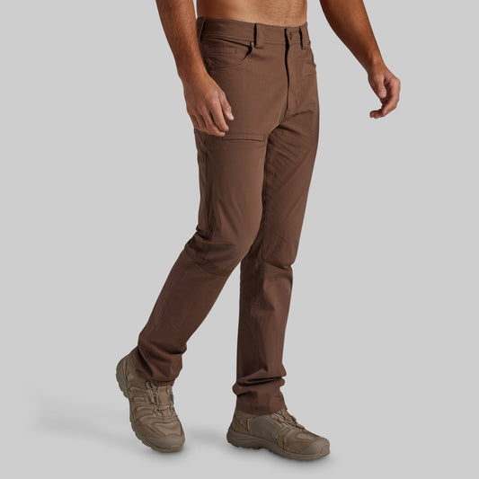 A man wearing brown cargo pants and brown boots, shown from the waist down against a solid gray background.