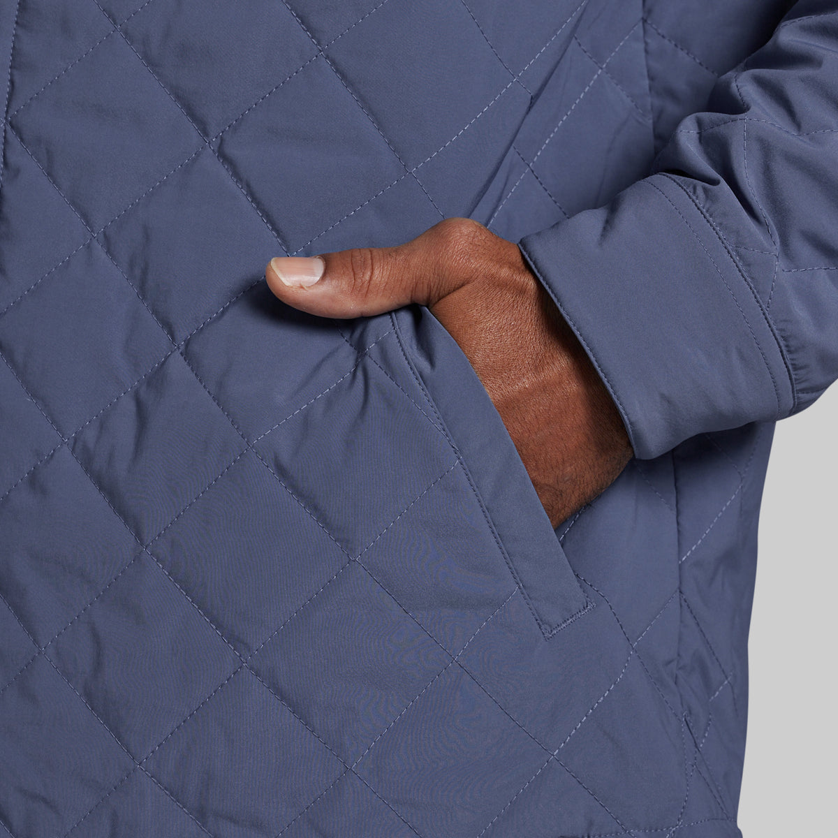 Close-up of a person wearing a quilted navy jacket, with a hand reaching into a side pocket.
