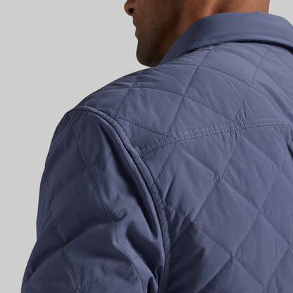 Close-up of a man wearing a navy blue diamond-quilted jacket, showing the texture and stitching on the shoulder and collar against a light gray background.