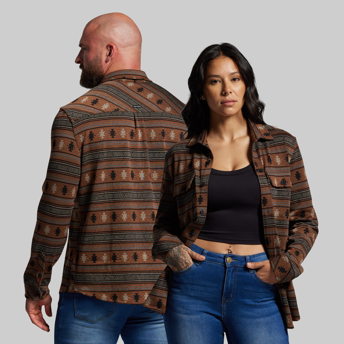 Man and woman wearing patterned shirts and jeans on a plain background