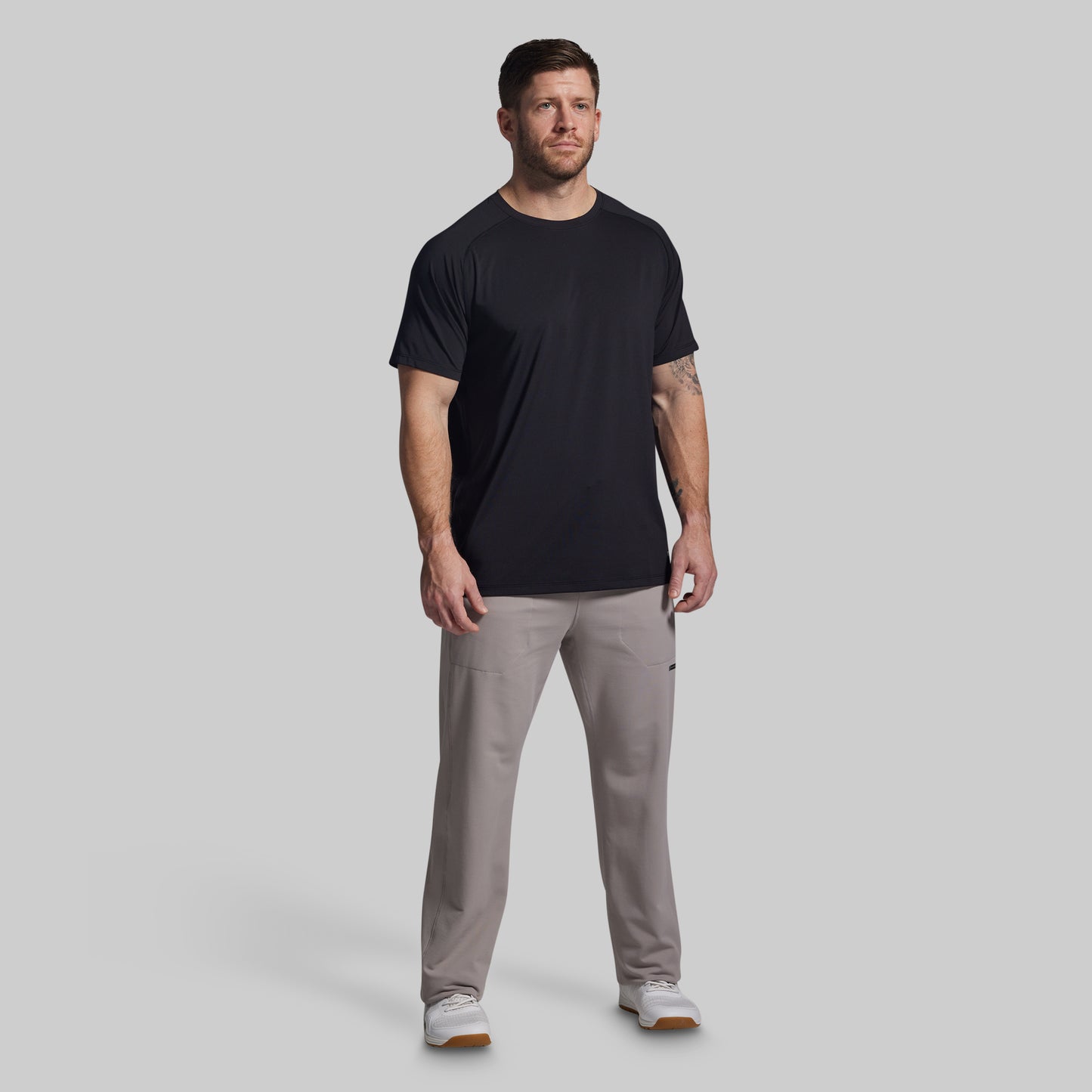 Man wearing a black t-shirt and gray pants on a light gray background