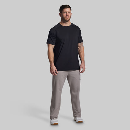 Man wearing a black t-shirt and gray pants on a light gray background