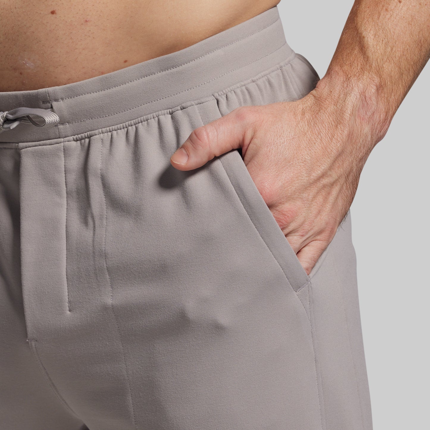 Close-up of gray pants with a hand in pocket on a neutral background