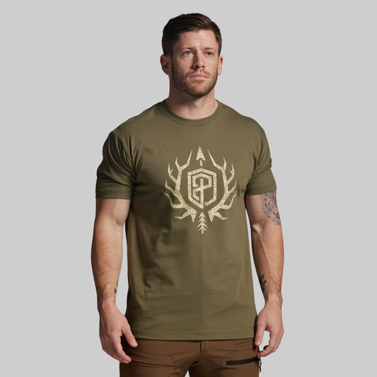 Man wearing an olive green t-shirt with a logo on a plain background
