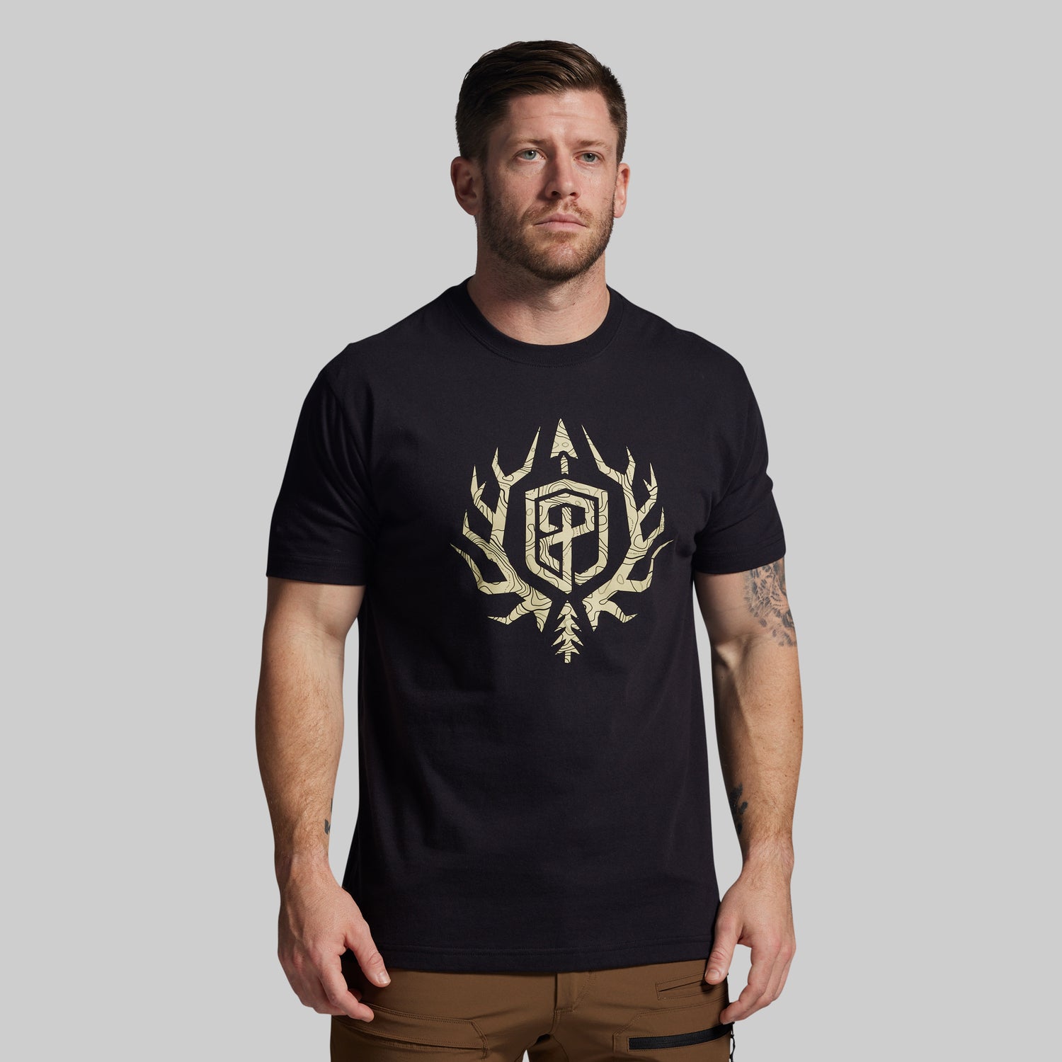 Man wearing a black t-shirt with a gold logo on a gray background