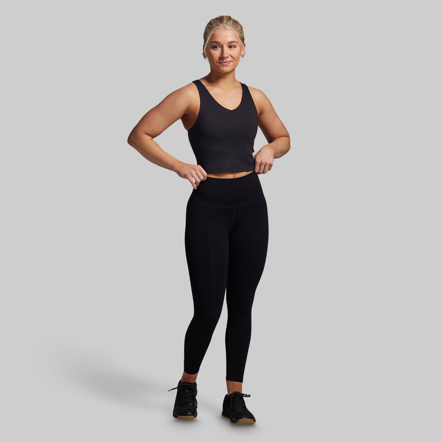 Woman wearing a black tank top and leggings on a gray background