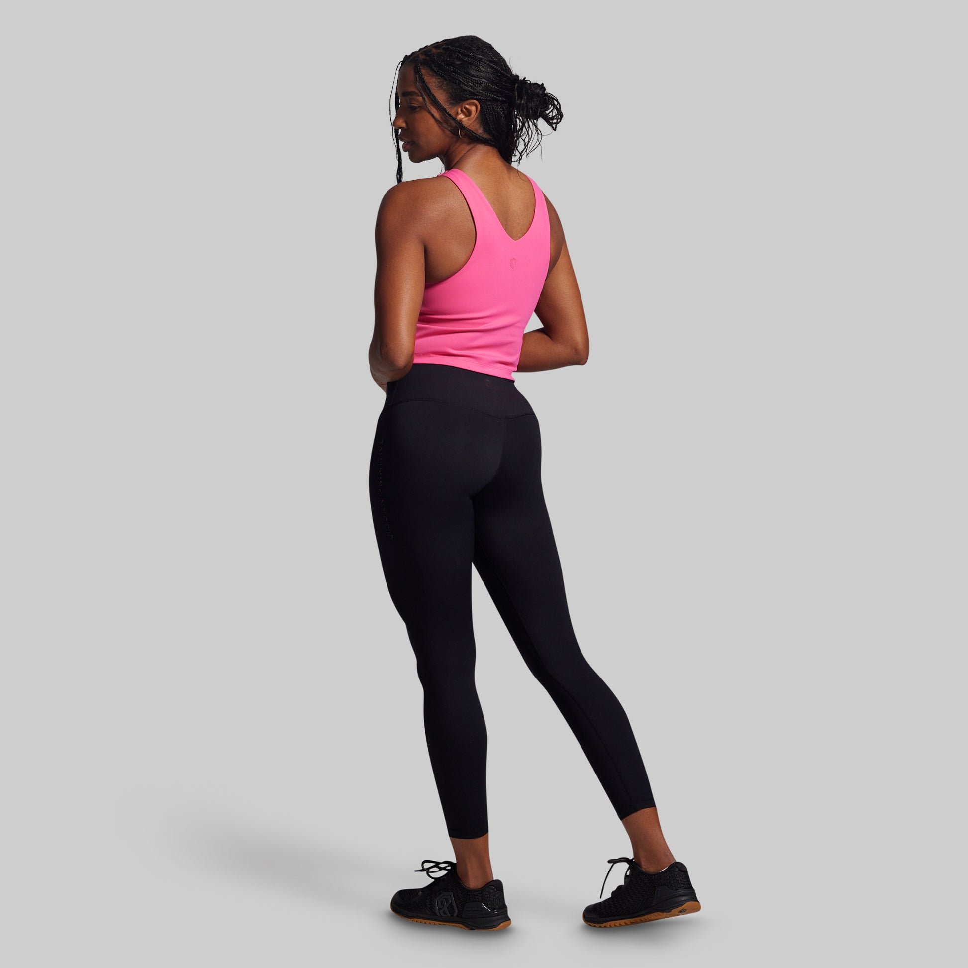 Woman wearing a pink tank top and black leggings on a gray background