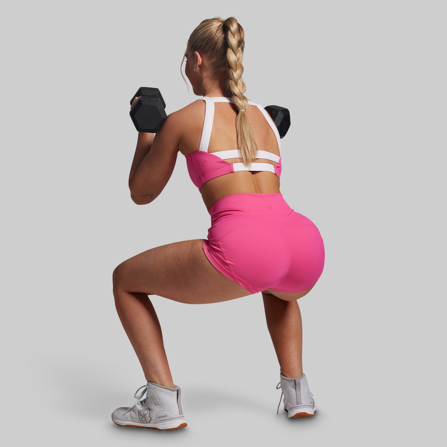 Woman in pink athletic outfit performing a squat with dumbbells on a gray background