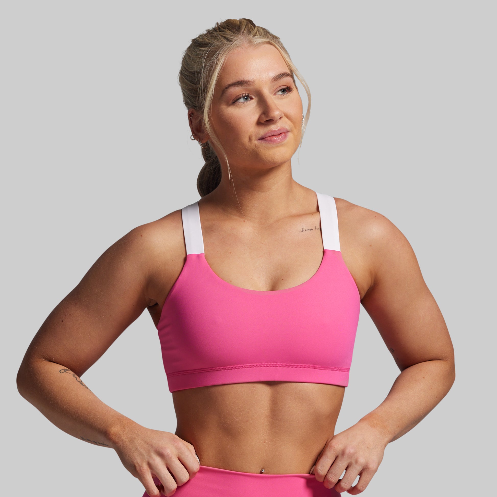 Woman wearing a pink sports bra and leggings on a gray background