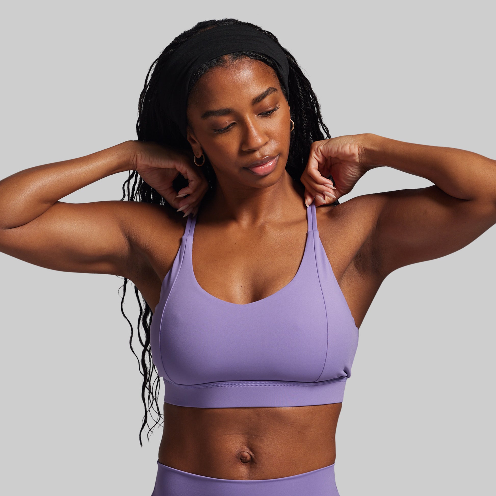 Woman wearing a purple sports bra and leggings against a gray background