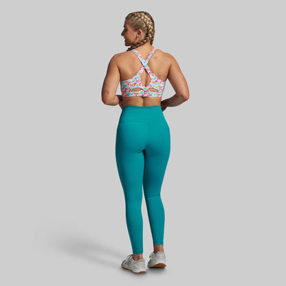 Woman wearing a colorful sports bra and teal leggings on a gray background