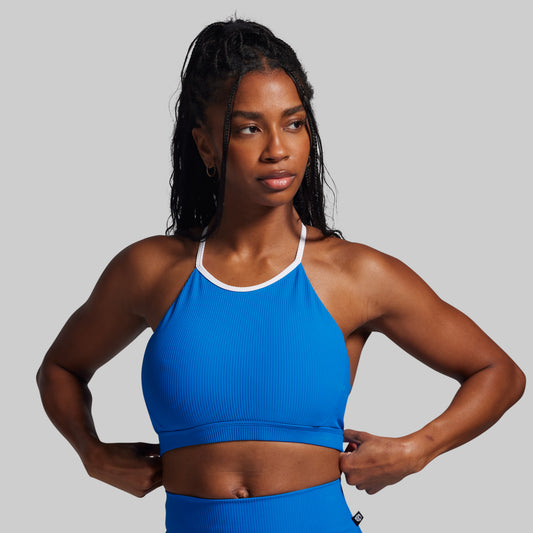 Woman wearing a blue sports bra and leggings on a gray background