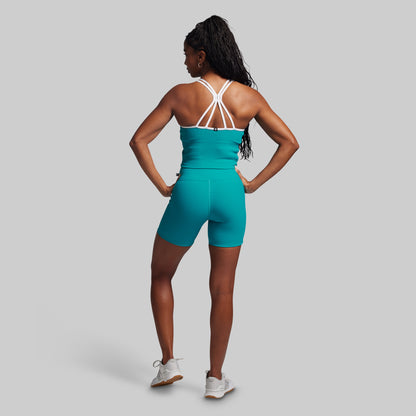 Woman wearing a teal athletic outfit with white straps on a gray background