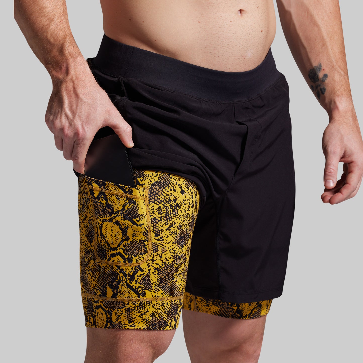 Person wearing black shorts with yellow snake print trim on a plain background