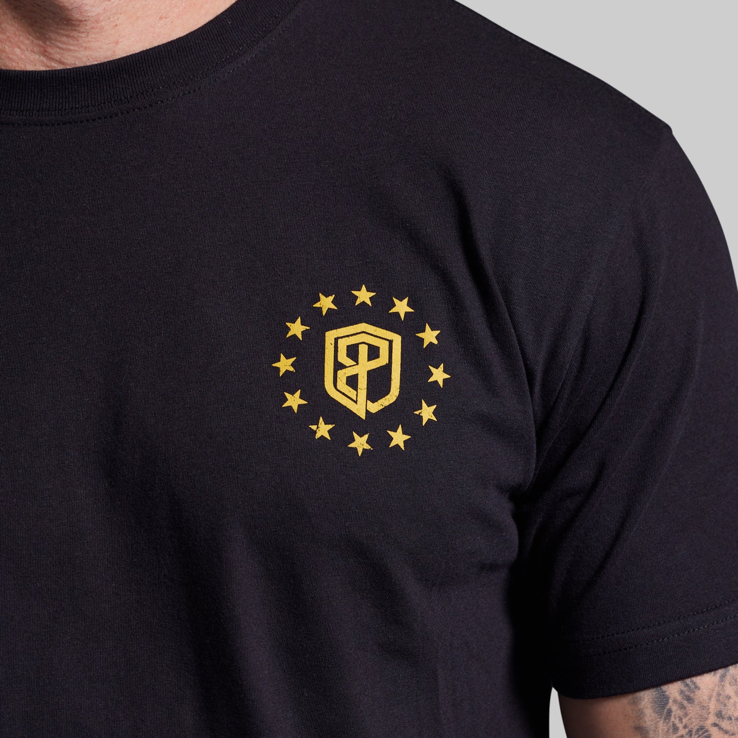 Black t-shirt with a yellow emblem featuring a shield and stars on a gray background