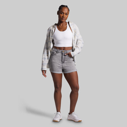 Woman wearing a white crop top, plaid shirt, gray shorts, and white sneakers on a light gray background