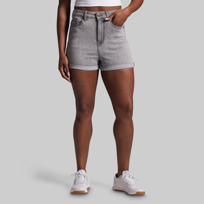 Person wearing gray shorts and white sneakers on a plain background