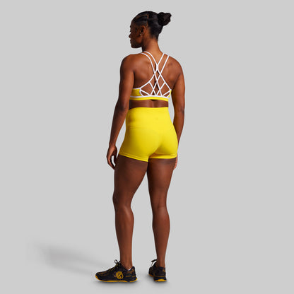 Person wearing a yellow athletic outfit with a white sports bra on a gray background