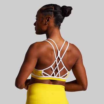 Woman wearing a white strappy top and yellow shorts on a gray background