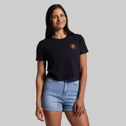 Woman wearing a black t-shirt with a yellow logo and light blue shorts on a gray background
