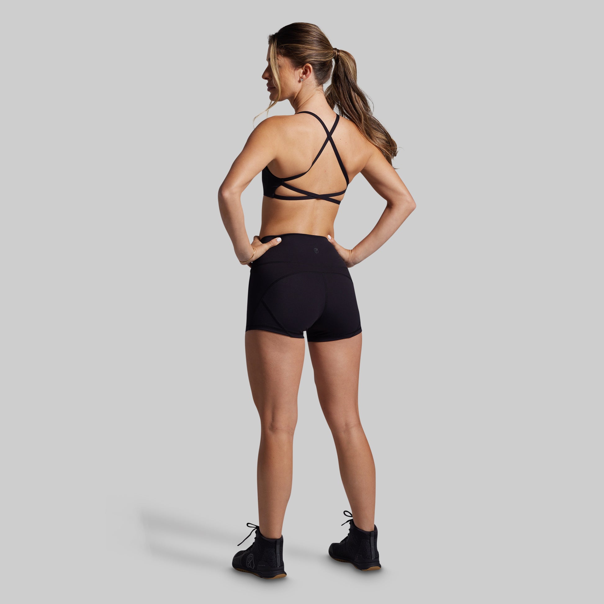 Woman wearing a black sports bra and shorts on a gray background