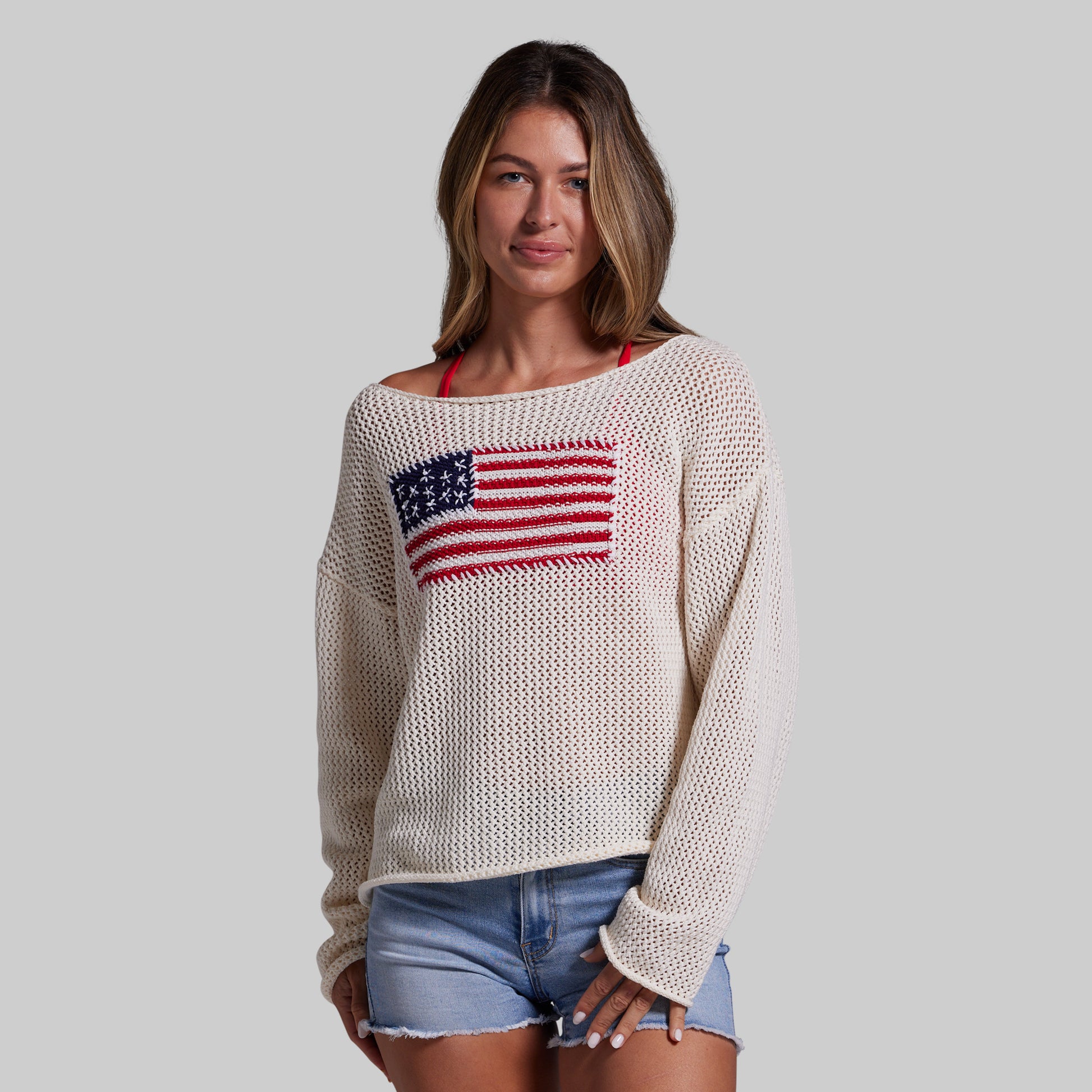 Woman wearing a cream sweater with an American flag design on a gray background