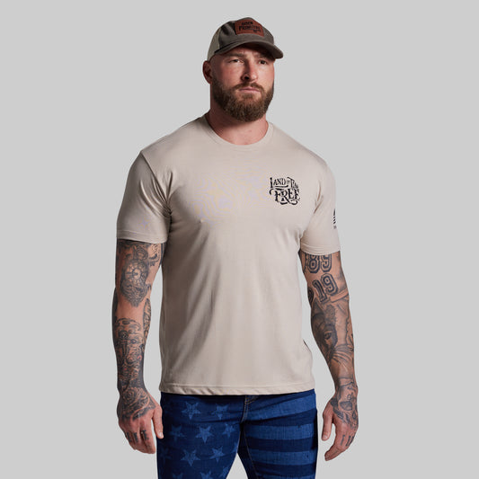 Man wearing a beige t-shirt with a logo and blue pants with star patterns on a gray background