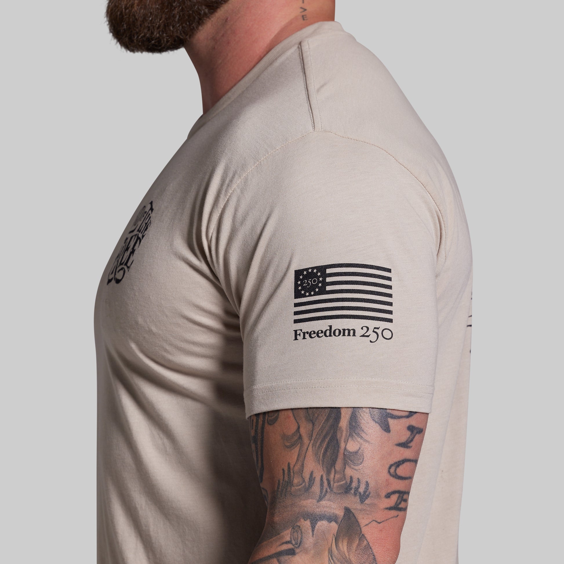 Man wearing a beige t-shirt with an American flag design and text on a plain background