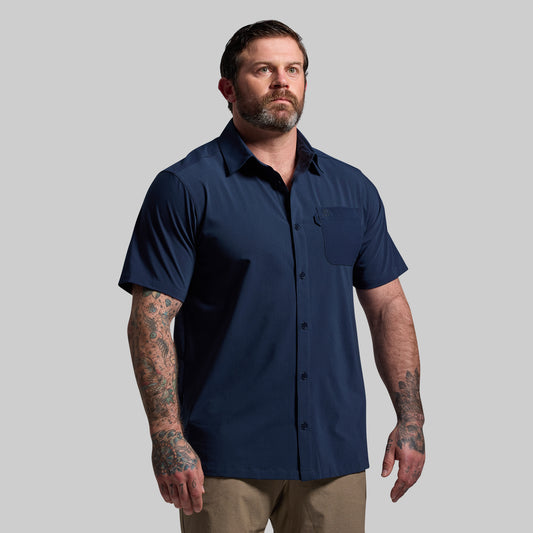 A man wearing a navy blue button-up shirt with short sleeves, collar, and a chest pocket.