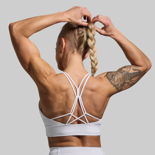 Person wearing a white sports bra with criss-cross straps against a gray background