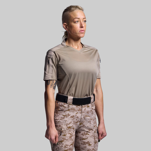 Person wearing a beige tactical shirt and camouflage pants on a gray background