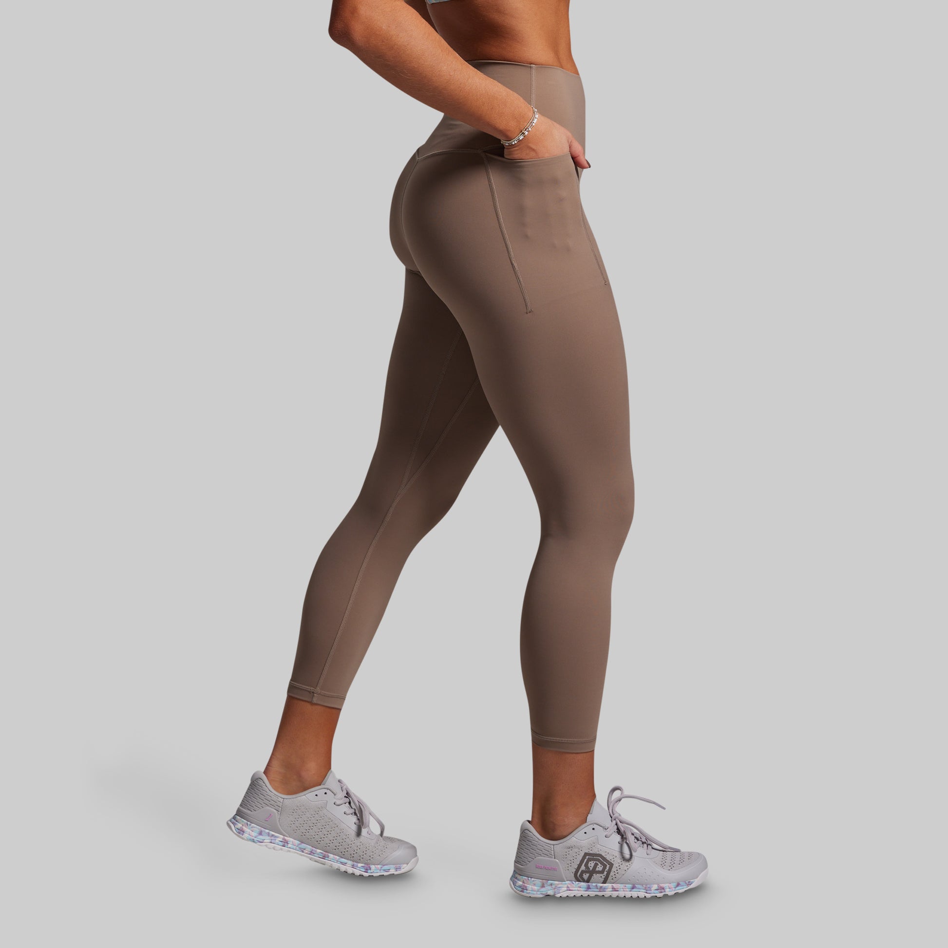 Person wearing beige leggings and gray sneakers on a plain background