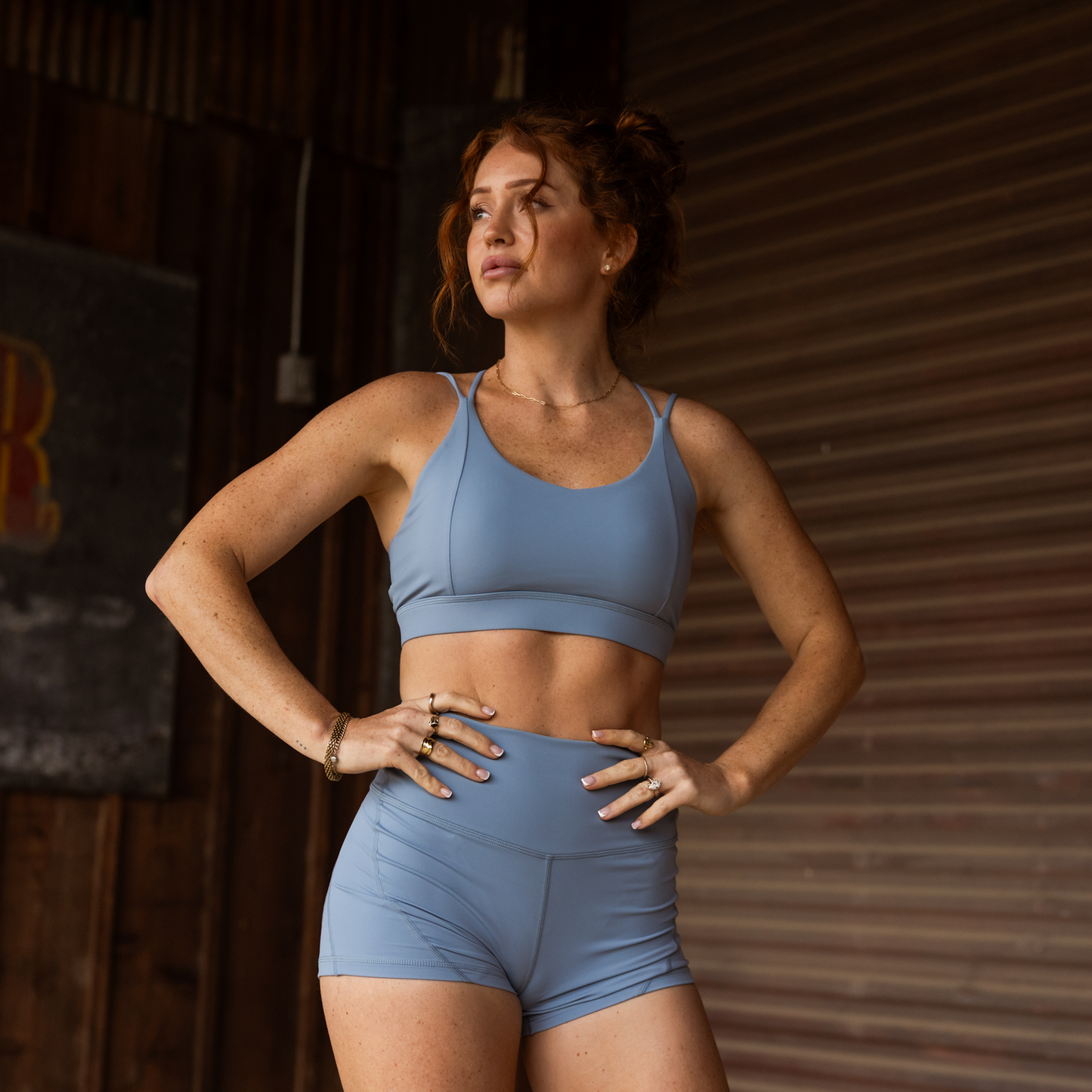 Woman wearing a blue sports bra and shorts in a rustic setting