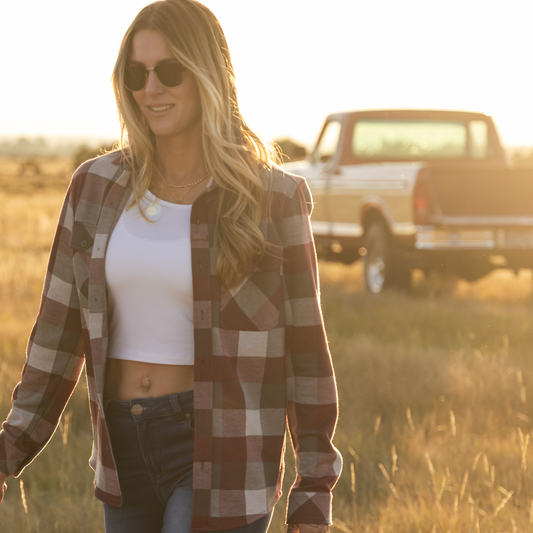 Woman wearing a plaid shirt and sunglasses in a field with a truck in the background