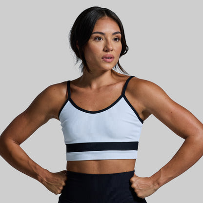 Woman wearing a white sports bra with black straps and trim on a gray background