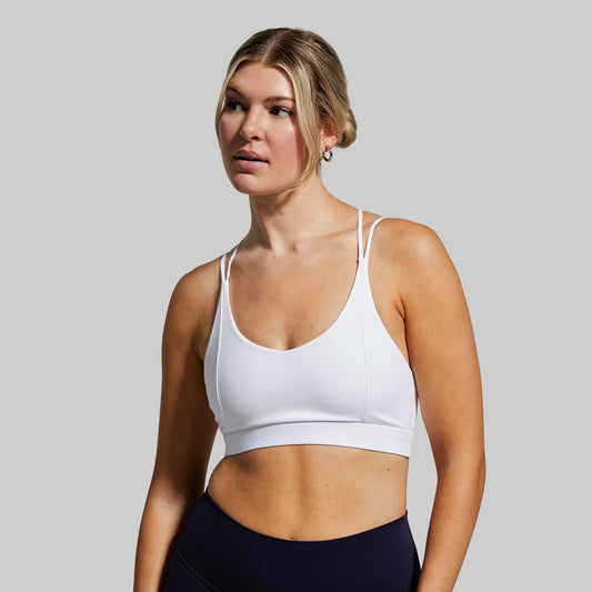 Woman wearing a white sports bra and black leggings against a gray background