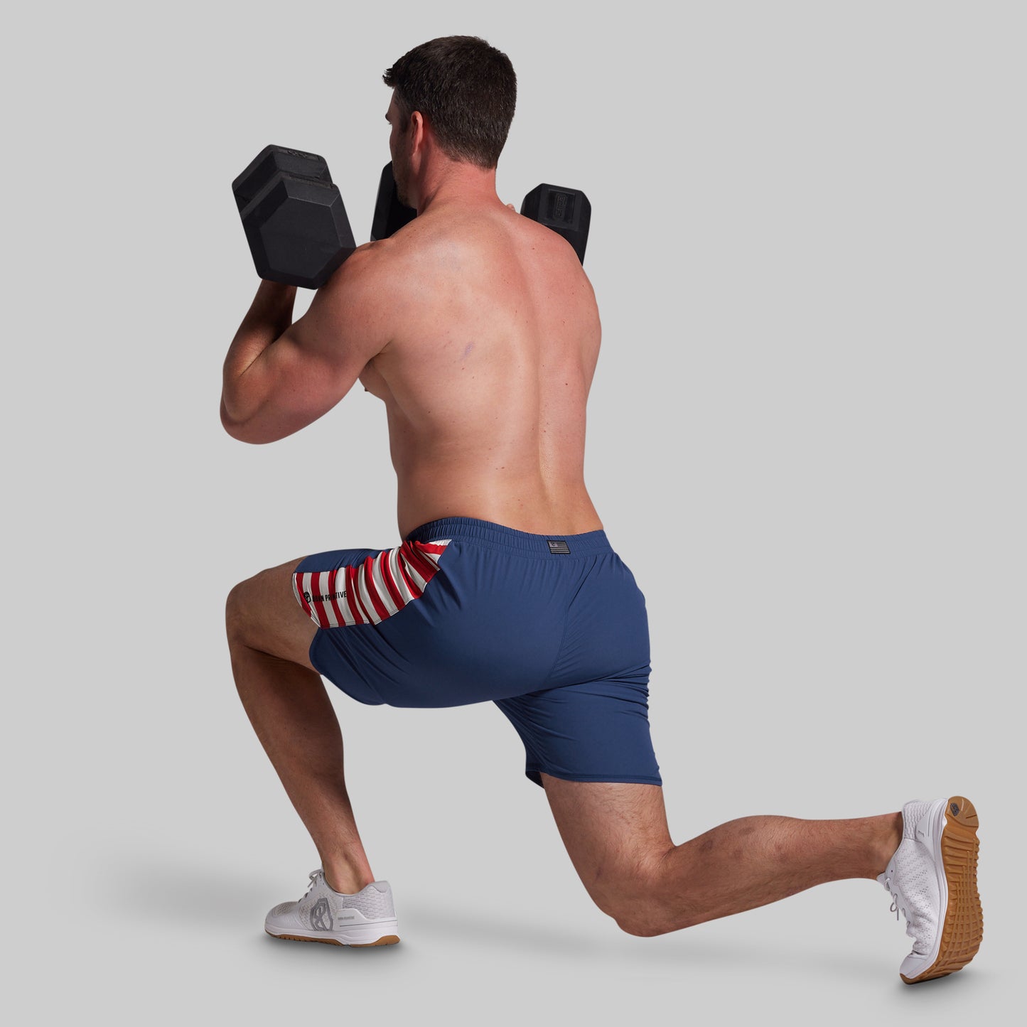 Man performing a lunge with dumbbells wearing blue shorts with a red, white, and blue pattern.