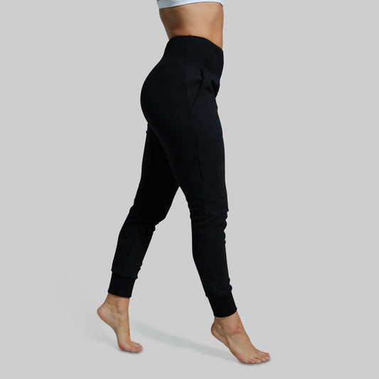 Side view of a woman wearing black high-waisted joggers with a textured pattern.