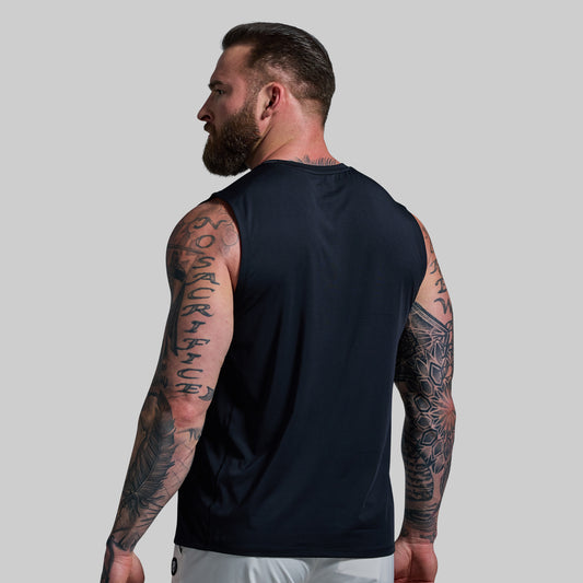 Man wearing a black sleeveless shirt with tattoos on arms against a gray background