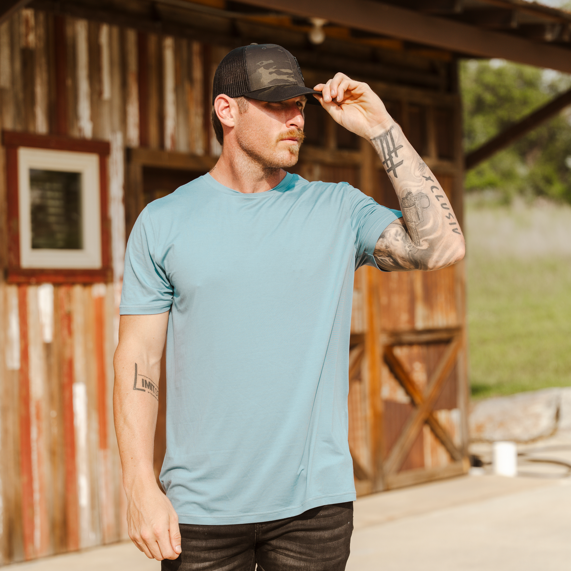 Man wearing a blue t-shirt and black cap outdoors near a wooden structure