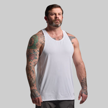 Man wearing a white tank top with tattoos on arms against a gray background