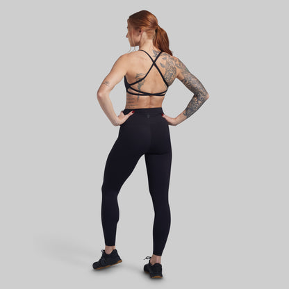 Woman wearing black athletic leggings and sports bra on a gray background