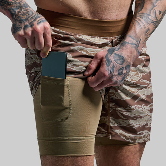 A person wearing camouflage patterned versatile shorts with a compression liner and a phone held in the pocket.