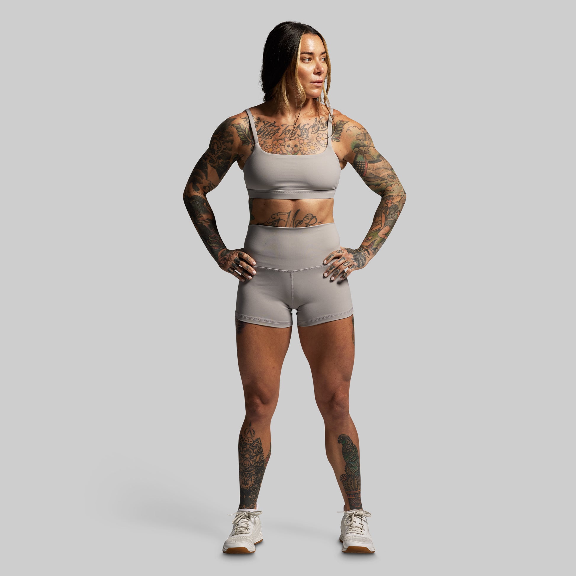 Woman wearing a gray athletic outfit with tattoos on a plain background