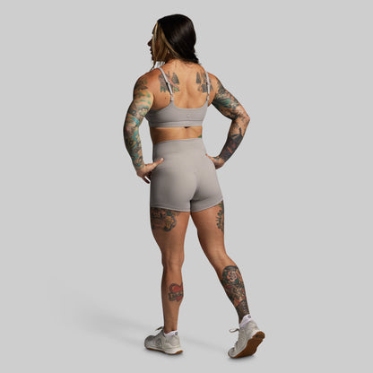 Person wearing a gray sports bra and shorts set on a plain background