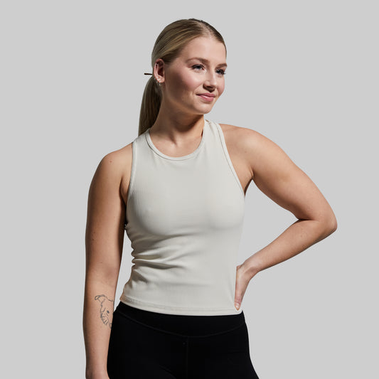 A woman wearing a sleeveless ribbed beige tank top with a built-in bra, paired with black pants.