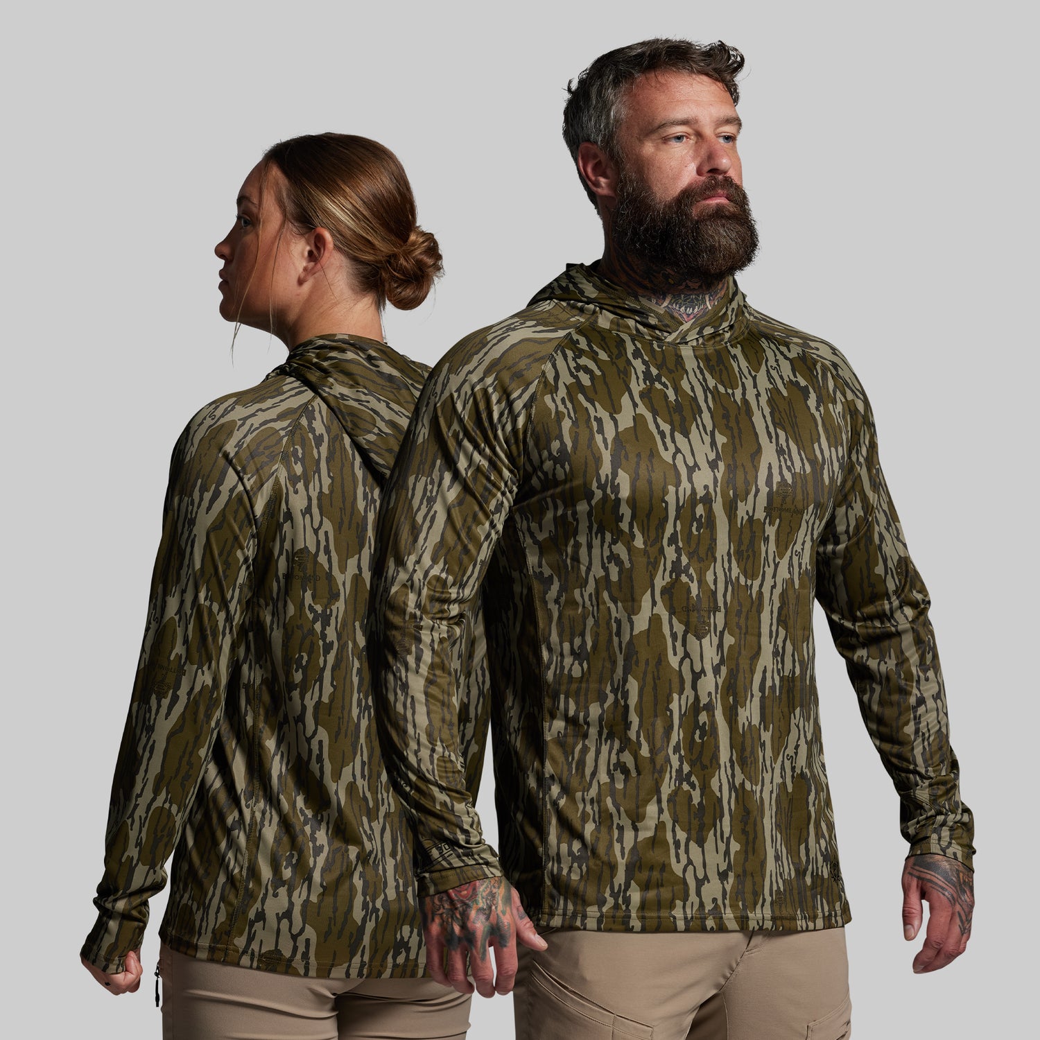 Two people wearing camouflage hoodies on a plain background