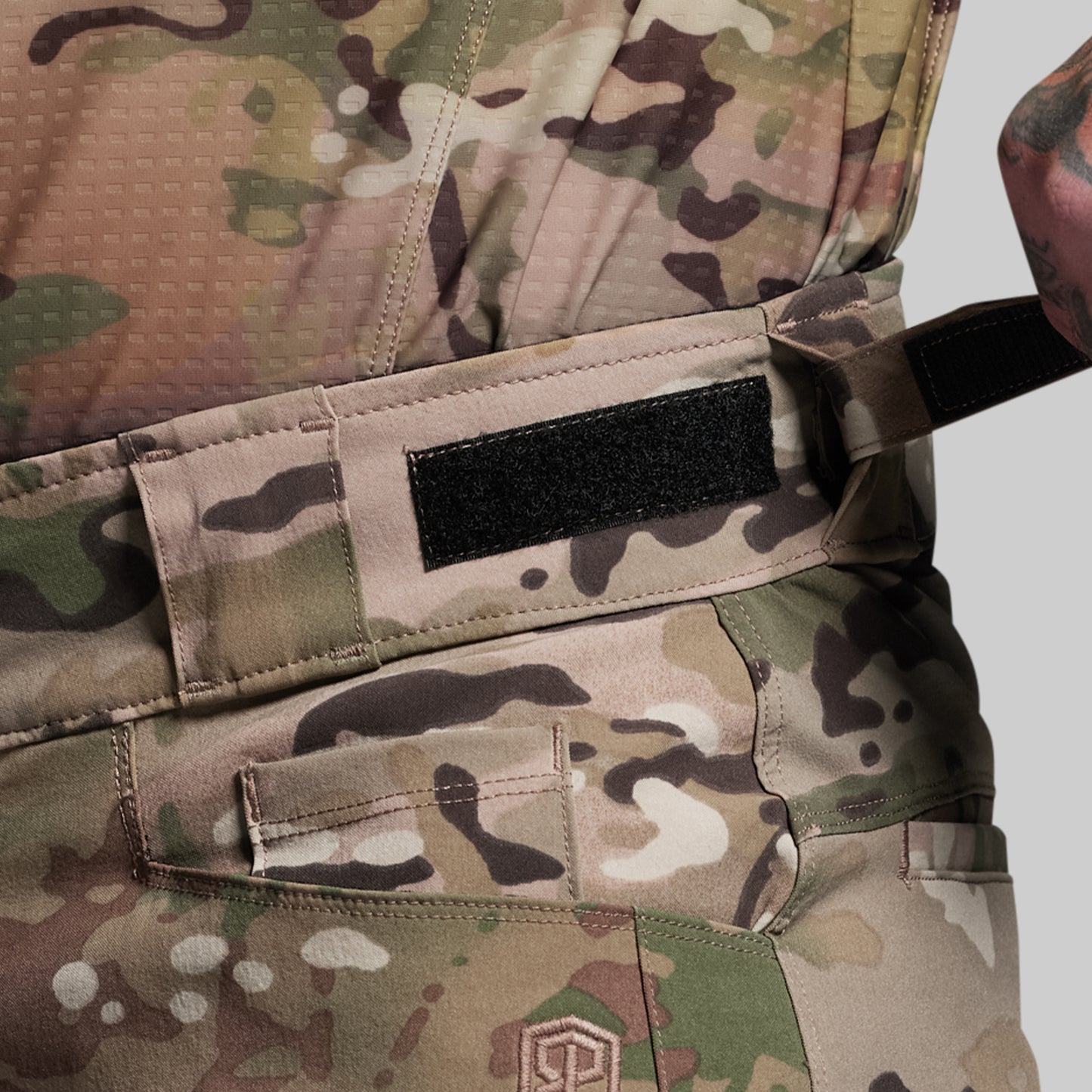 Close-up of a camouflage military uniform with a visible brand logo on a gray background